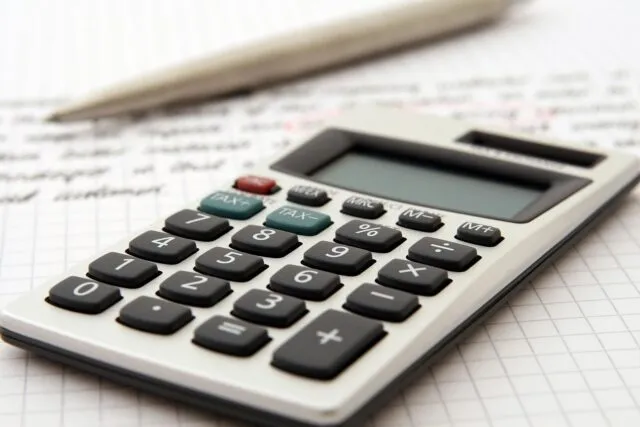 Calculator, caiet și o cană de cafea pe un birou, în timpul unui calcul de buget